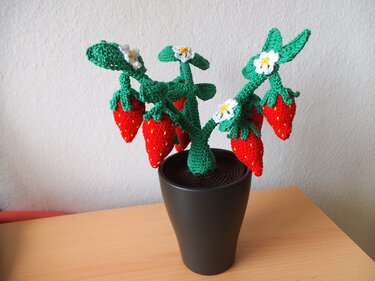 Gehäkelte Erdbeerpflanze mit roten Erdbeeren, weißen Blüten und dunklem Topf