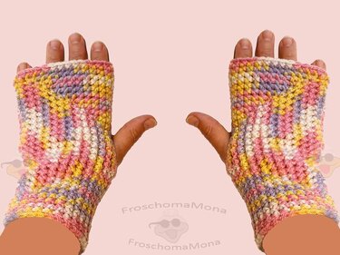 Fingerlose, gehäkelte Handschuhe in Rosa, Gelb, Lila und Weiß an zwei Händen.