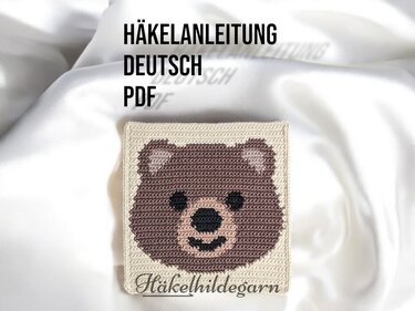 Gehäkeltes Pixelquadrat mit braunem Bärenkopf auf hellbeigem Untergrund