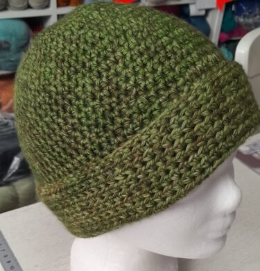 Gehäkelte grüne Beanie mit umgeschlagenem Rand auf weißem Kopfmodell, seitlich aufgenommen