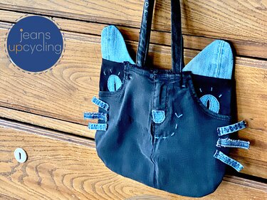 Katzenförmige Einkaufstasche aus Jeansstoff mit hellblauen Ohren und Jeansteilen, vor einer Holzkommode hängend