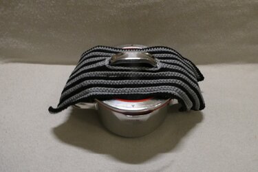 Gehäkelter Topflappen mit schwarzen und grauen Streifen über einem Topfdeckel