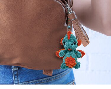 Teal and orange crocheted dinosaur keychain hanging from brown leather bag strap