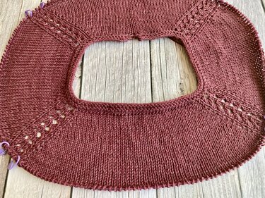 Nahaufnahme einer kastanienroten, von oben gestrickten Rundpasse mit Raglanzunahmen und Maschenmarkierern