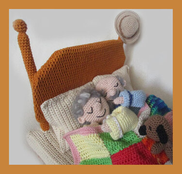 Cozy handmade amigurumi scene of an elderly couple sleeping under a crocheted patchwork blanket with a small dog beside them