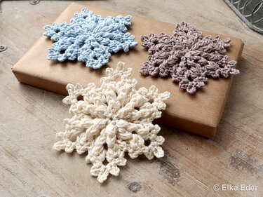 Three small fast-to-crochet snowflake motifs in cream, blue, and taupe on wrapped gift