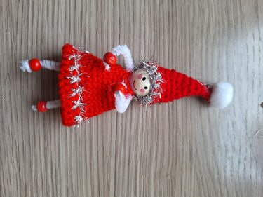 Gehäkelter roter Wichtel mit Holzkopf, silbernem Lametta und Pfeifenreiniger-Beinen auf Holzuntergrund