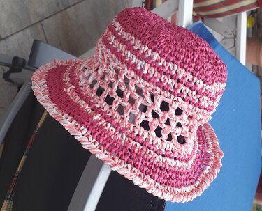 Gehäkelter Kinderhut in Pink und Weiß mit Lochmuster auf blauer Oberfläche