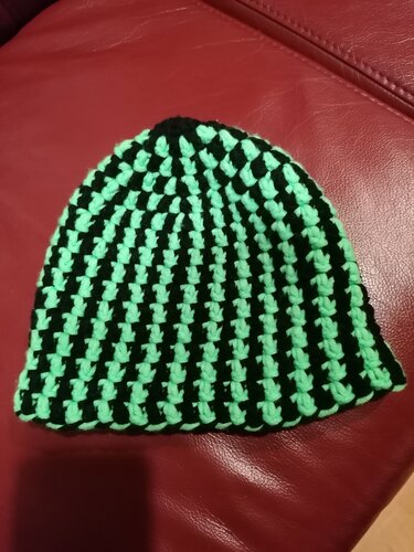 Gehäkelte Kinderbeanie in Schwarz und Mintgrün mit vertikalen Streifen auf rotem Untergrund