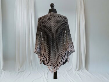 Triangular crochet shawl in gray ombre with open mesh stitch and scalloped lace border on a black dress form