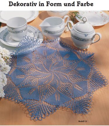 Blaues gehäkeltes Deckchen mit sternförmigem Muster auf Holztisch neben Porzellangeschirr