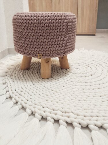 Gehäkelter Pouf mit Holzfüßen auf rundem Häkelteppich mit Quasten