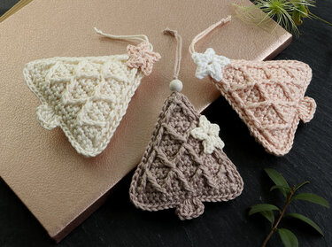 Three small crocheted tree decorations in cream, taupe and blush with star appliques, hanging loops and a wooden bead.