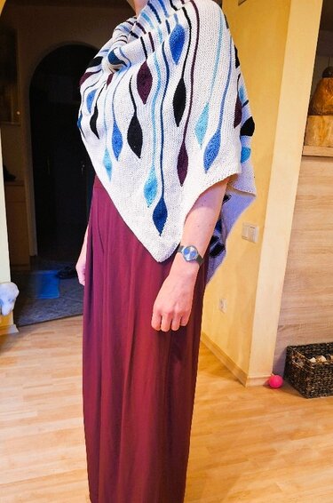 Gestricktes weißes Dreieckstuch mit blau-violetten Tropfenmotiven über einem bordeauxfarbenen Maxikleid