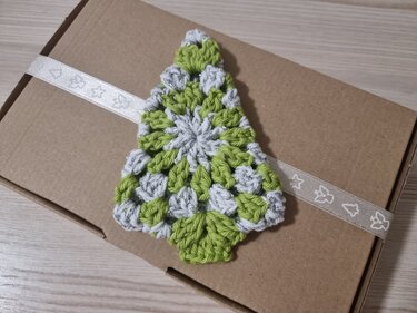 Gehäkelter Weihnachtsbaum in Grün und Silber auf brauner Geschenkbox mit Band.