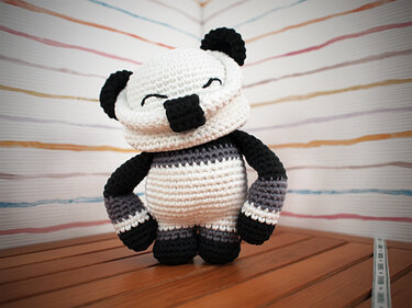 Gehäkelter Amigurumi-Panda in Schwarz, Weiß und Grau mit Streifen, stehend auf Holz