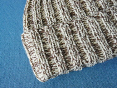 Strickmütze mit meliertem Garn in Braun und Beige im Rippenmuster auf blauem Hintergrund