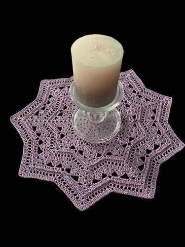 Lavender star-shaped crocheted shawlette with lace pattern under a pillar candle on a black background