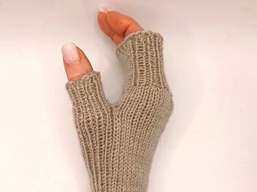 Beigefarbener, gestrickter fingerloser Handschuh an einer Hand mit sichtbaren Rippenbündchen.