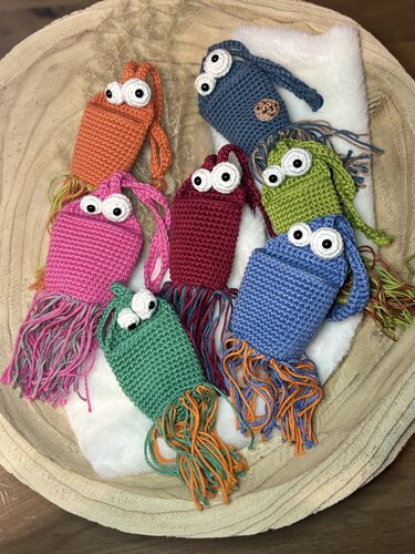Mehrere verspielte, farbige Amigurumi-Beutel mit großen Augen und Quasten dekorativ in einer Schale gelegt