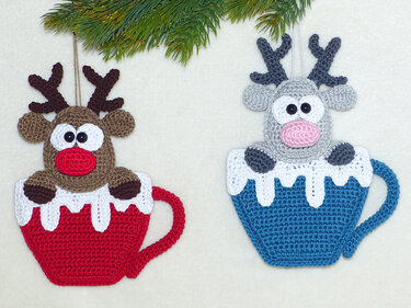 Two crocheted reindeer ornaments in red and blue crochet mugs with white snow trim, antlers and hanging loops