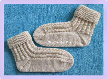 Paar hellbeiger gestrickter Babysocken mit umgeschlagenem Bündchen auf blauem Untergrund