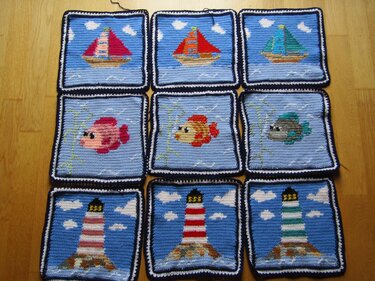 Neun gehäkelte Pixelquadrate mit Segelboot-, Fisch- und Leuchtturm‑Motiven auf blauem Grund