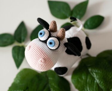 Detailed view of crocheted amigurumi cow showing horns, ears, tail tuft and spot layout