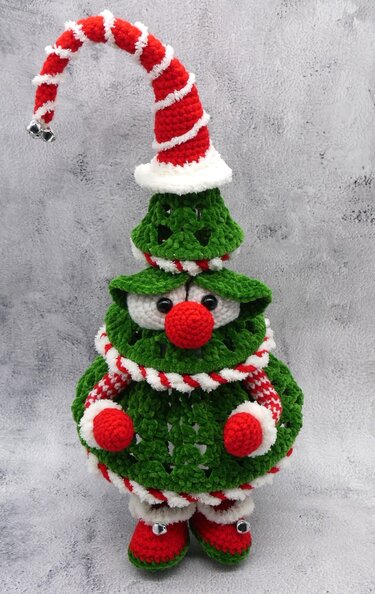 Gehäkelter Weihnachtsbaum-Wichtel in Grün, Rot und Weiß mit gestreifter Zipfelmütze und roter Nase.