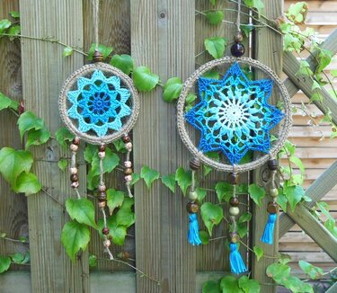 Zwei gehäkelte Traumfänger in Blau und Weiß mit Holzperlen an einem Holzzaun mit Efeu