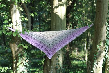 Triangular lace crochet shawl in lilac-to-cream gradient stretched between trees