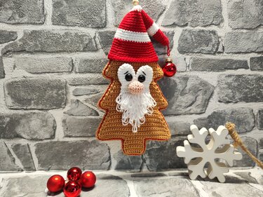 Gehäkeltes Tannenbaum-Amigurumi mit Weihnachtsmann-Gesicht, Schlaufenbart und rot-weißer Mütze, hängend vor Ziegelwand