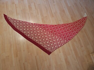 Gestricktes Dreieckstuch in Rot und Creme mit Zickzackmuster, flach auf hellem Holzboden ausgebreitet