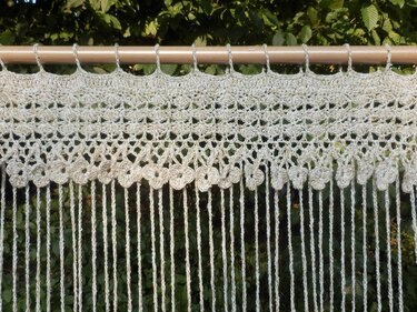 Beiger Häkelvorhang mit Aufhängeschlaufen, Blumenborte und langen Fransen an einer Holzstange