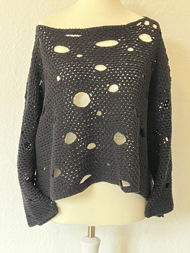 Dunkelgrauer gehäkelter Damenpullover mit unregelmäßigen Löchern und weitem U‑Boot‑Ausschnitt auf einer Schaufensterpuppe.