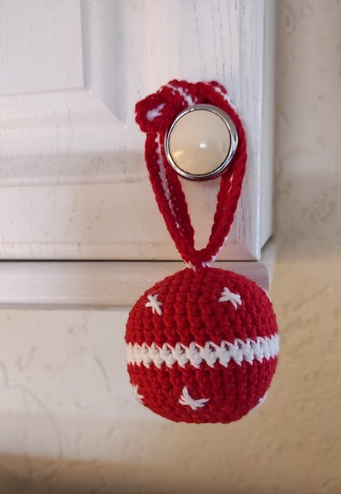 Rote gehäkelte Weihnachtskugel mit weißem Streifen und Schlaufe an einem Möbelknopf