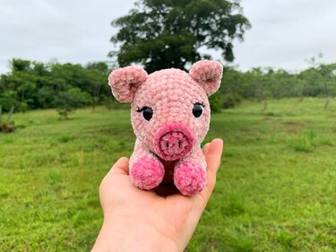 Rosa kuscheliges Amigurumi-Glücksschweinchen, handgehalten vor Naturhintergrund
