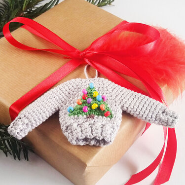 Gehäkelter grauer Mini-Pullover mit Weihnachtsbaum aus bunten Perlen und Aufhängeschlaufe, auf Geschenk platziert