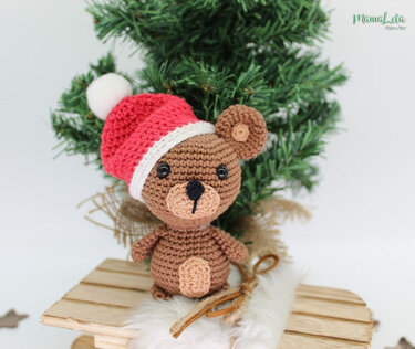 Gehäkelter brauner Teddy mit roter Weihnachtsmütze vor kleinem Tannenbaum