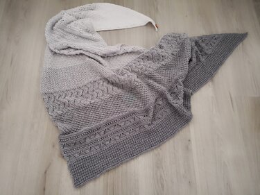 Gestricktes graues Dreieckstuch mit Farbverlauf und unterschiedlichen Musterstreifen auf hellem Boden