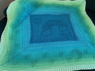 Gehäkelte Babydecke in Grün‑Blau mit mittigem Regenbogenmotiv und Noppenmuster