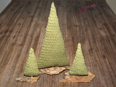 Three green crocheted cone Christmas trees on bark on a wooden table