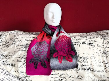Gehäkelter Schal in Pink, Grau und Schwarz mit Rosenmuster auf einer Schaufensterpuppe vor roter Wand