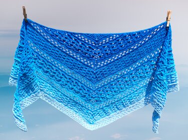 Gehäkeltes blaues Dreieckstuch mit Farbverlauf und offenem Lochmuster an einer Wäscheleine vor klarem Himmel