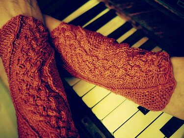 Rostrote gestrickte Armstulpen mit Zopfmuster auf Klaviertasten