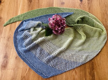 Gestricktes Dreieckstuch Blau-Grün mit Lochmuster und rosa Hortensie auf Holztisch