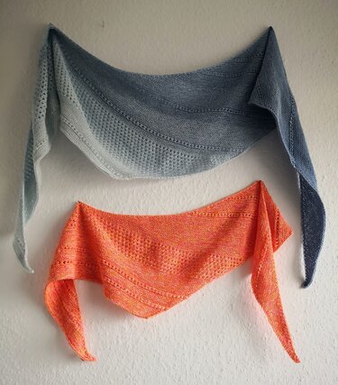 Zwei gestrickte Dreieckstücher an weißer Wand, oben blau-grau, unten orange