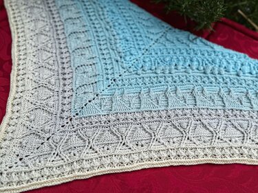 Crocheted triangle shawl ombre grey to blue with cables and bobble stitches on red background