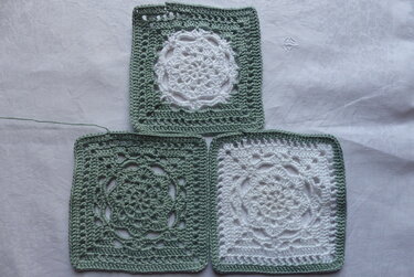 Drei gehäkelte Granny Squares in Grün und Weiß auf hellem Stoff
