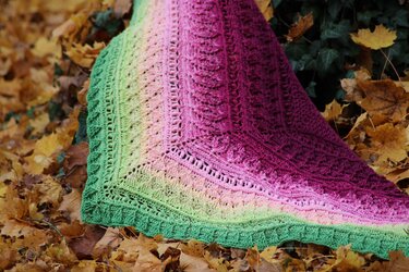 Crocheted triangle shawl with green-to-magenta ombre and lace stitches on autumn leaves.